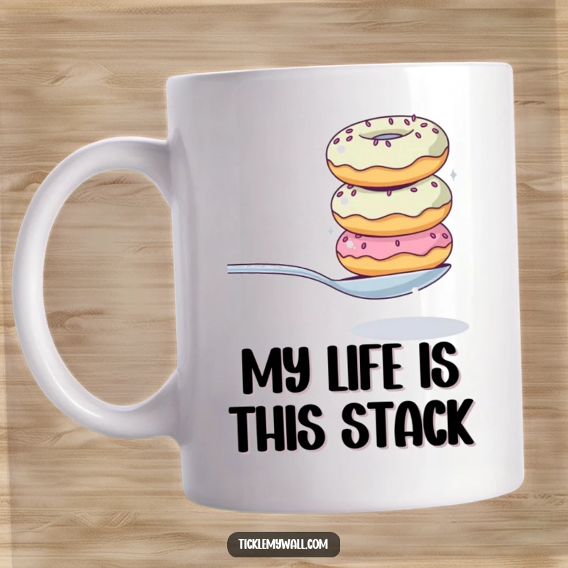Funny mug showing a precarious stack of donuts wobbling while attempting to balance a single spoon, a humorous depiction of a sweet struggle.